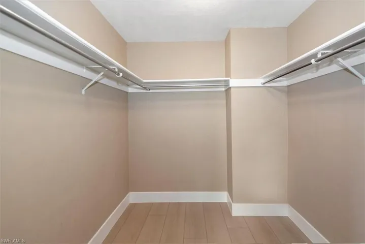 Walk-in closet featuring light wood-finish flooring, white baseboards, and comprehensive built-in shelving with hanging rods
