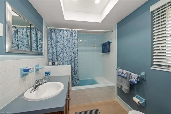 Bathroom featuring a vanity with an integrated sink, a rectangular mirror with a silver-toned frame, a tiled shower-tub combination, and a skylight