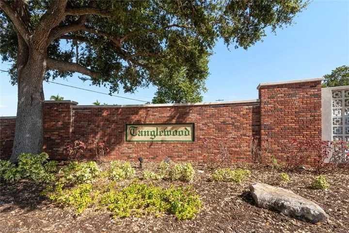 Brick entry wall with a "Tanglewood" sign, featuring a mature tree, varied landscaping, and decorative concrete block screening