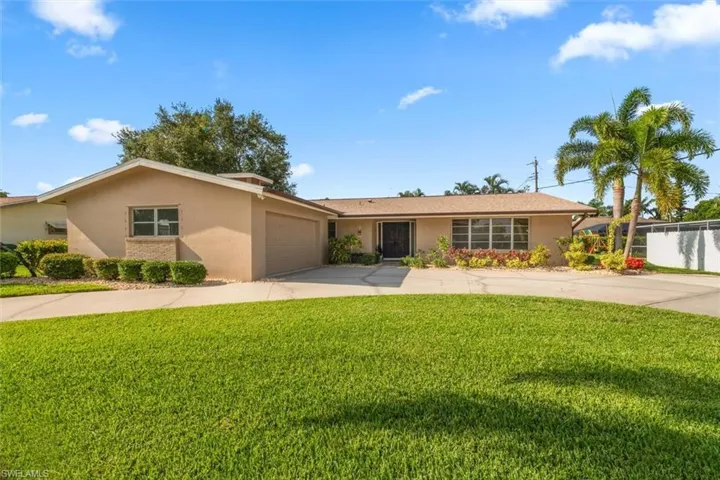 Single-story residence featuring a two-car garage, front lawn, mature landscaping, and an extended driveway