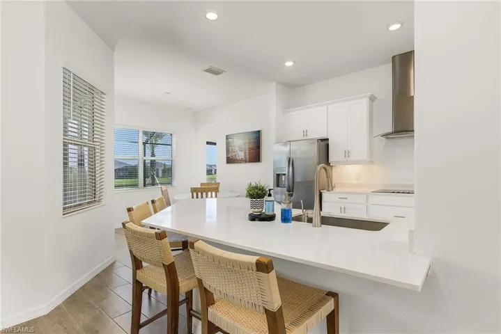 Kitchen featuring a breakfast bar, white cabinets, stainless steel fridge, wall chimney range hood, and recessed lighting