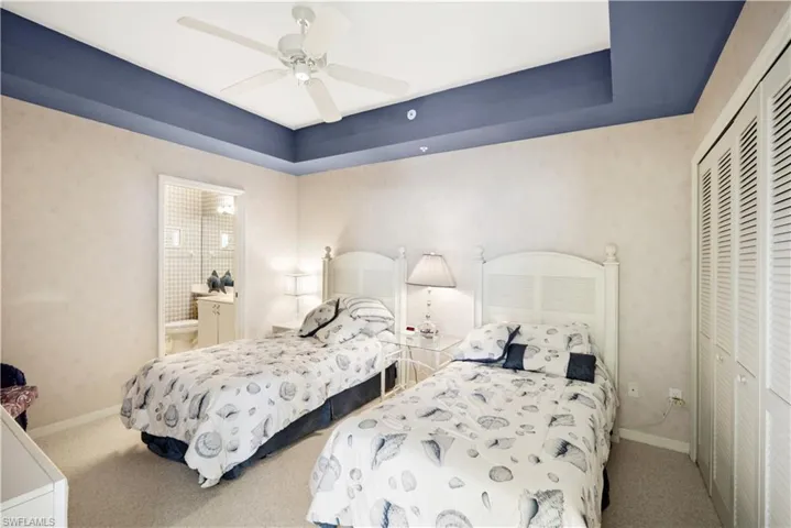 Carpeted bedroom with ceiling fan, a raised ceiling, and a closet
