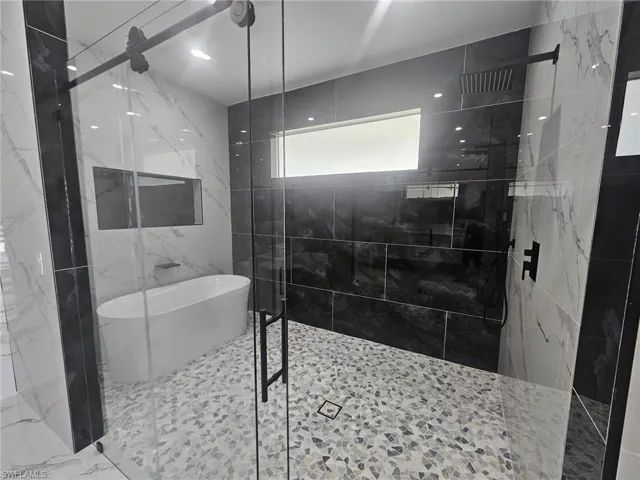 Full bathroom featuring a soaking tub, a marble finish shower, and tile walls
