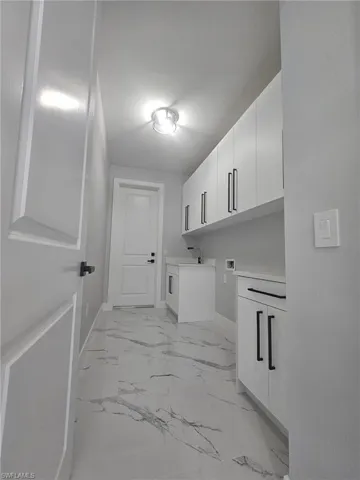 Washroom featuring hookup for a washing machine, baseboards, marble finish floor, and cabinet space
