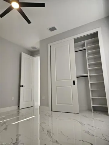 Unfurnished bedroom with a ceiling fan, a closet, marble finish floor, baseboards, and visible vents