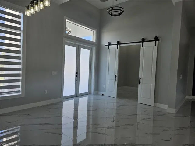 Foyer entrance featuring a barn door, a high ceiling, marble finish floor, french doors, and baseboards