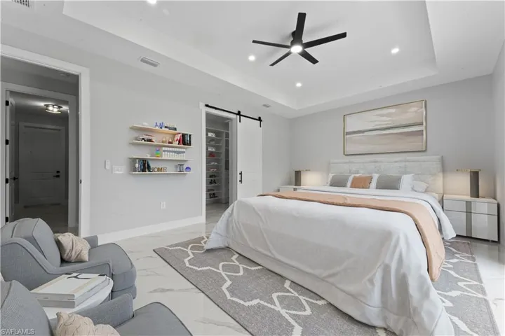 Bedroom featuring a tray ceiling, a barn door, recessed lighting, marble finish floor, and a walk in closet