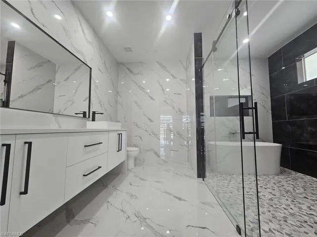 Bathroom featuring marble finish floor, toilet, vanity, tile walls, and stone wall