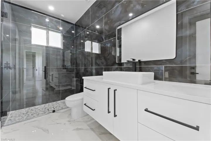 Bathroom featuring a stall shower, vanity, tile walls, marble finish floor, and toilet
