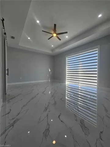 Empty room with a barn door, visible vents, a ceiling fan, marble finish floor, and a raised ceiling
