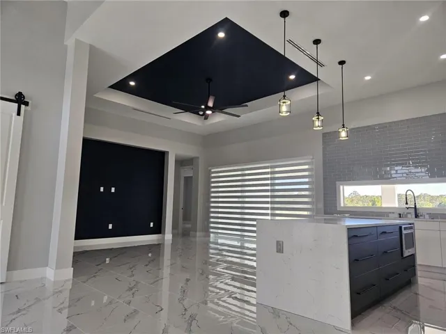 Unfurnished living room with baseboards, a ceiling fan, marble finish floor, and a tray ceiling