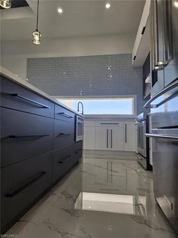 Kitchen featuring marble finish floor, oven, modern cabinets, refrigerator, and white cabinetry