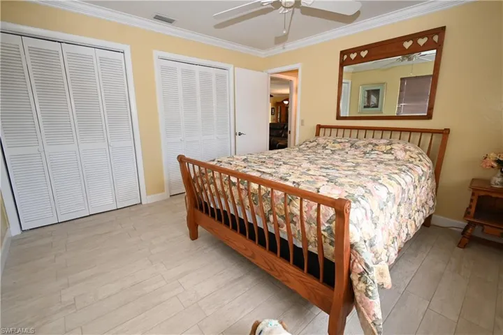 Bedroom featuring light-toned plank flooring, crown molding, and two louvered bifold closet doors