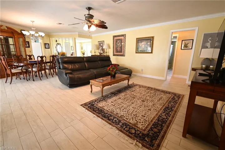 Open-concept living area with light-toned wood-finish flooring, a ceiling fan, crown molding, and a dining area with a chandelier