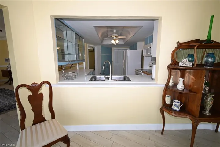 Kitchen pass-through featuring an undermount sink with a gooseneck faucet, light-toned countertop, and white cabinetry
