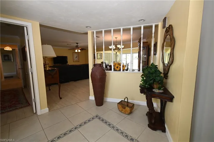Entryway featuring neutral-toned floor tile with decorative border, a half-wall with white balusters, and pale yellow wall paint