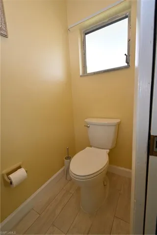 Powder room featuring a single-pane window, light-toned wall paint, white baseboards, and wood-finish tile flooring