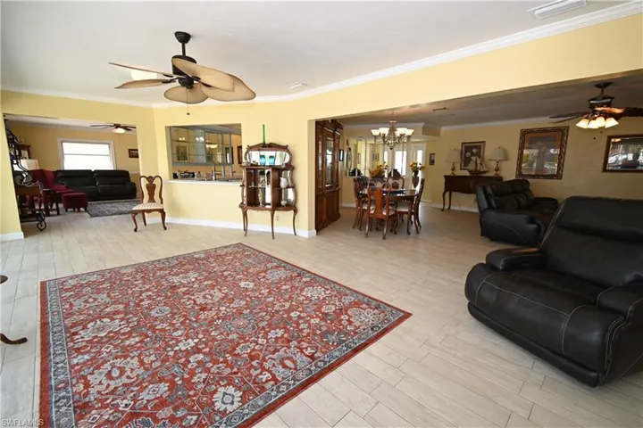 Spacious open-concept living area featuring light-toned plank flooring, a built-in kitchen pass-through, and multiple ceiling fans