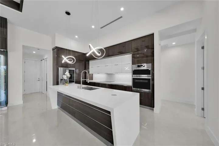 Kitchen with white cabinetry, sink, stainless steel appliances, decorative light fixtures, and a kitchen island with sink