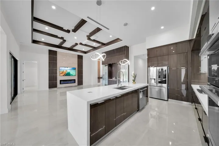 Kitchen featuring a kitchen island with sink, sink, a fireplace, decorative light fixtures, and stainless steel appliances