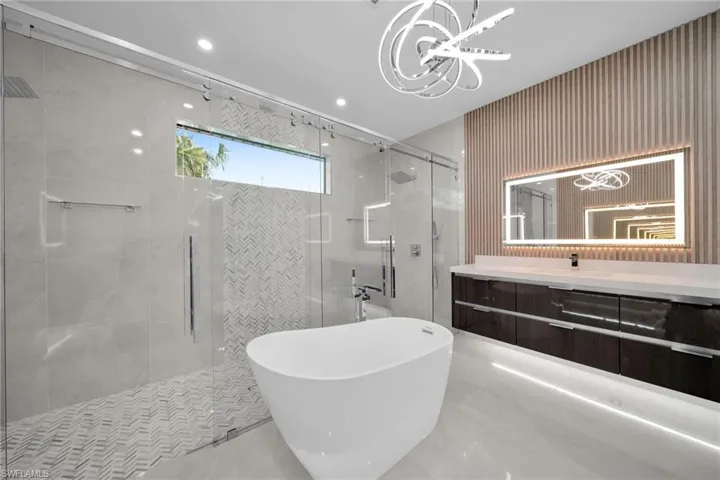 Bathroom with a notable chandelier, vanity, and shower with separate bathtub