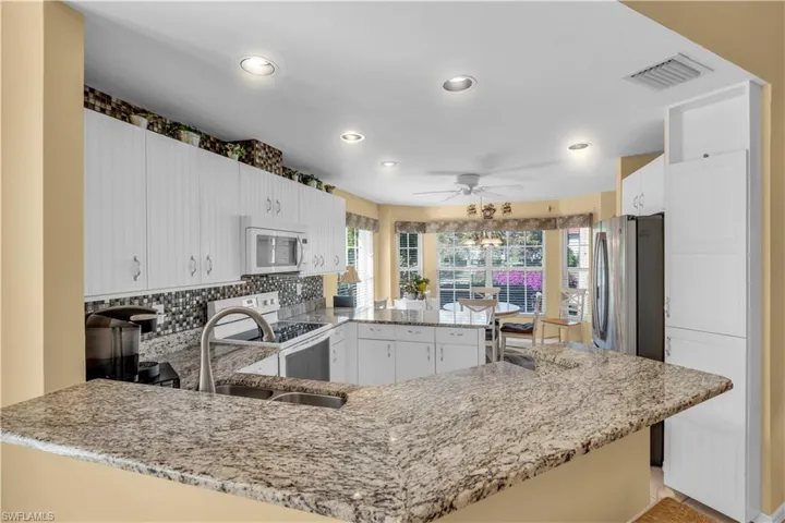 Kitchen with kitchen peninsula, stainless steel appliances, white cabinets, and a healthy amount of sunlight