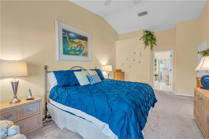 Bedroom featuring ceiling fan, light colored carpet, lofted ceiling, and ensuite bath