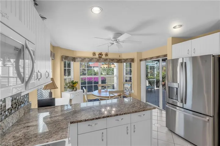 Kitchen featuring white cabinetry, stainless steel fridge, light tile patterned floors, and dark stone counters