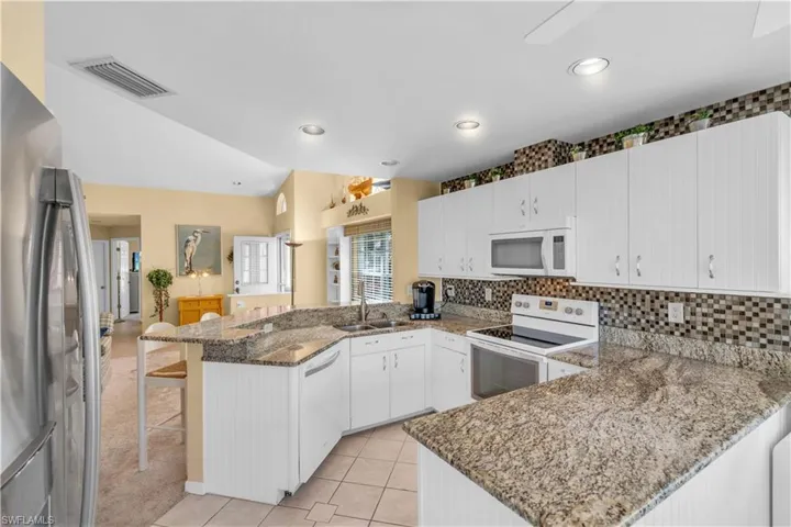 Kitchen featuring white appliances, dark stone counters, a kitchen breakfast bar, kitchen peninsula, and white cabinetry
