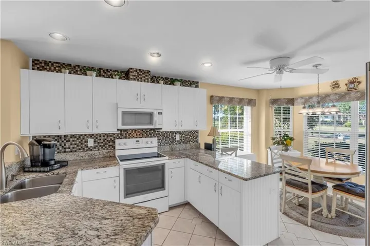 Kitchen with kitchen peninsula, white appliances, white cabinets, and sink