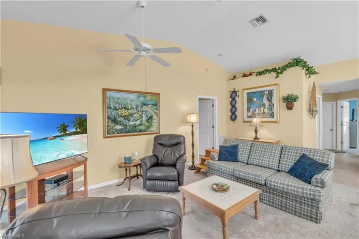 Living room featuring light colored carpet, high vaulted ceiling, and ceiling fan