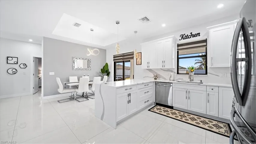 Kitchen with a raised ceiling, stainless steel appliances, a peninsula, pendant lighting, and light stone countertops