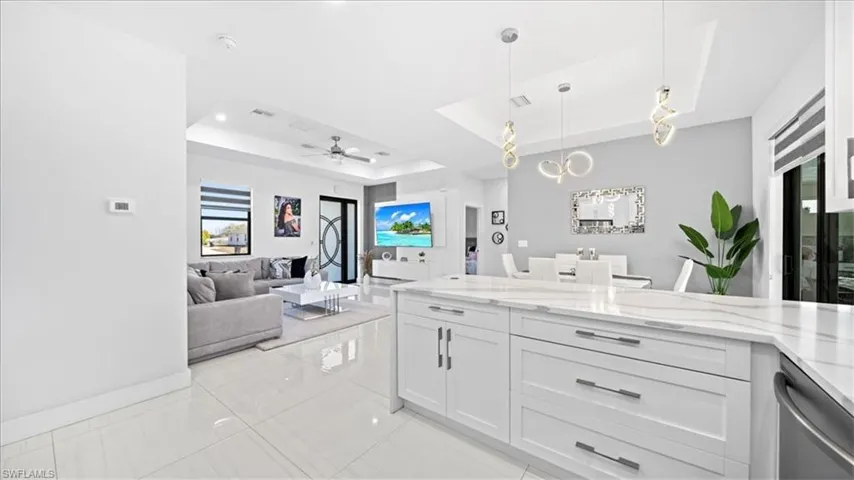 Kitchen featuring a tray ceiling, decorative light fixtures, light stone counters, dishwasher, and white cabinetry