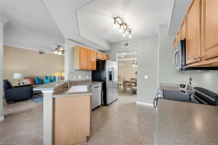 Kitchen featuring open floor plan, light brown cabinetry, a ceiling fan, a peninsula, and stainless steel appliances