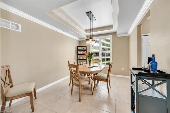 Dining space with a raised ceiling, ornamental molding, light tile patterned floors, and a chandelier