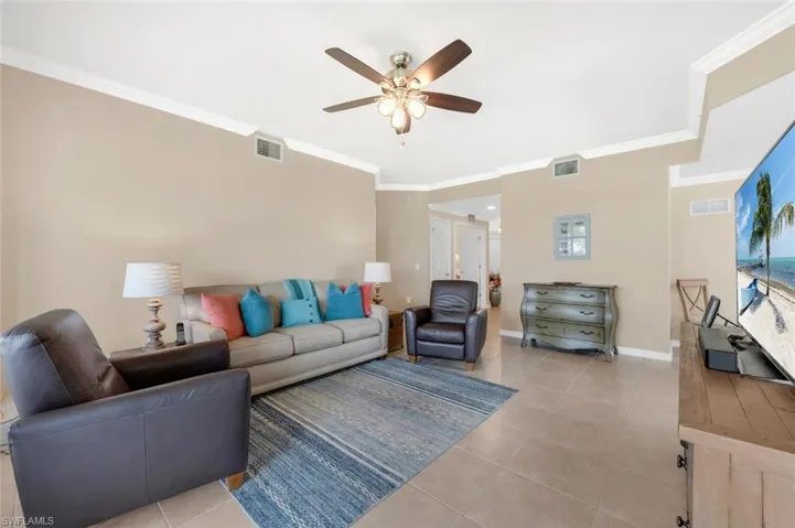 Living area with ceiling fan, crown molding, and light tile patterned floors