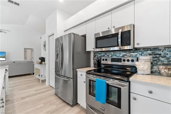 Kitchen featuring white cabinetry, backsplash, ceiling fan, stainless steel appliances, and light wood-type flooring