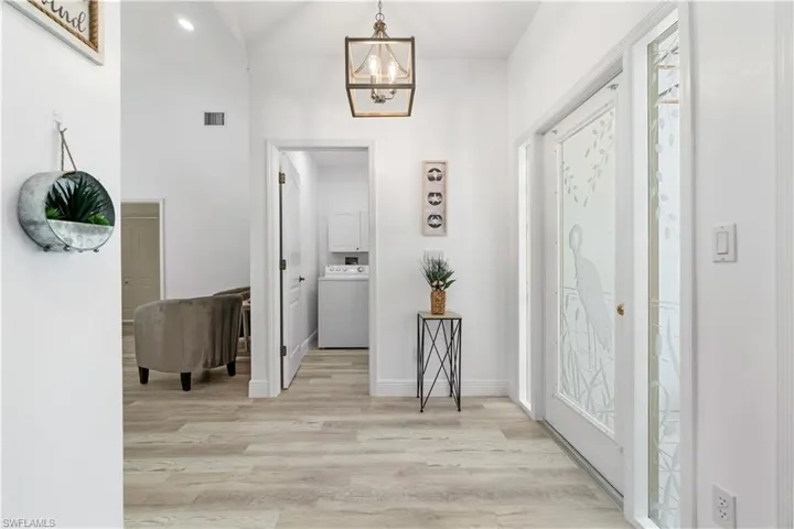 Foyer with lofted ceiling, washer / clothes dryer, a chandelier, and light hardwood / wood-style floors