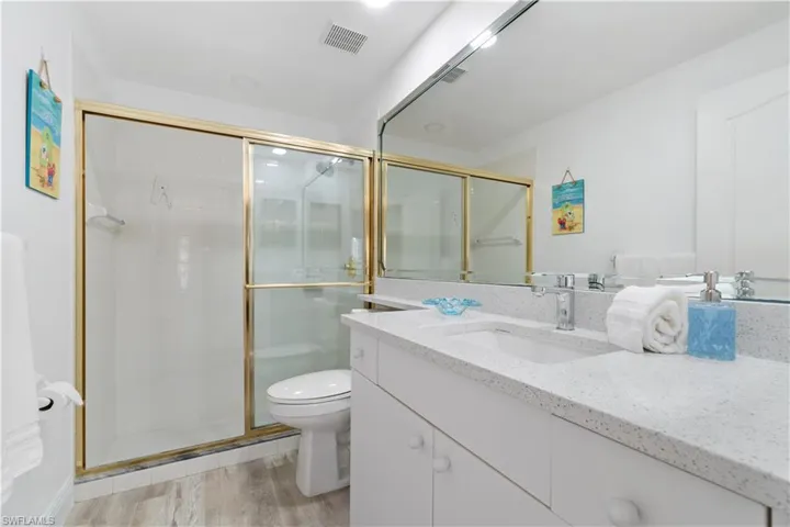 Bathroom with an enclosed shower, vanity, hardwood / wood-style flooring, and toilet