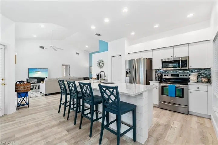 Kitchen featuring a breakfast bar, sink, white cabinetry, an island with sink, and stainless steel appliances