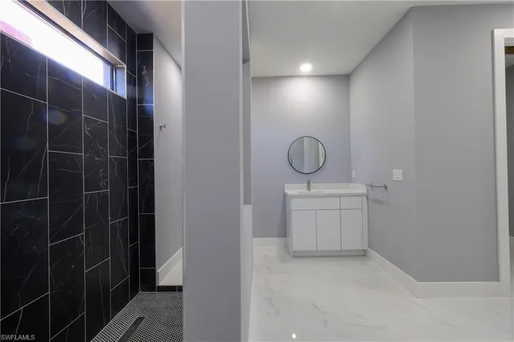 Full bath with light marble finish floors, a marble finish shower, and vanity