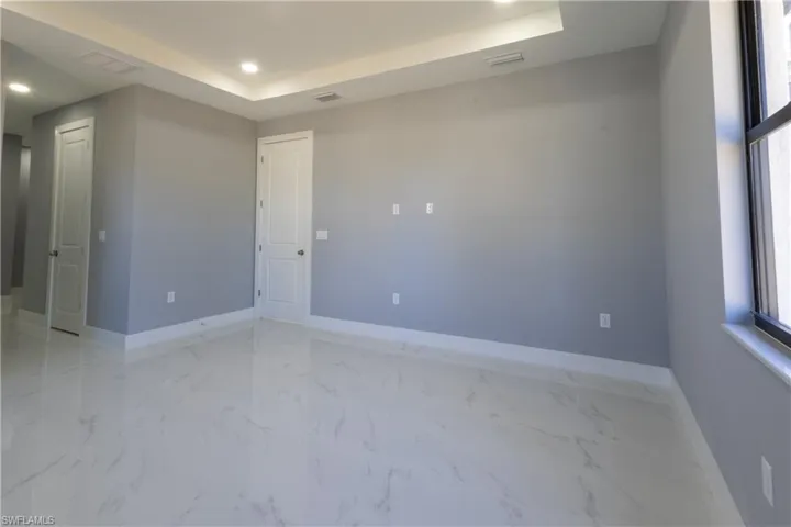 Empty room with recessed lighting, light marble finish floors, and a tray ceiling