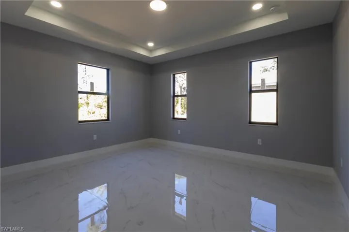 Empty room featuring marble tiled flooring, recessed lighting, and a raised ceiling