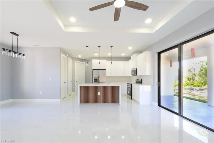 Kitchen featuring white cabinets, hanging light fixtures, a center island, stainless steel appliances, and a raised ceiling