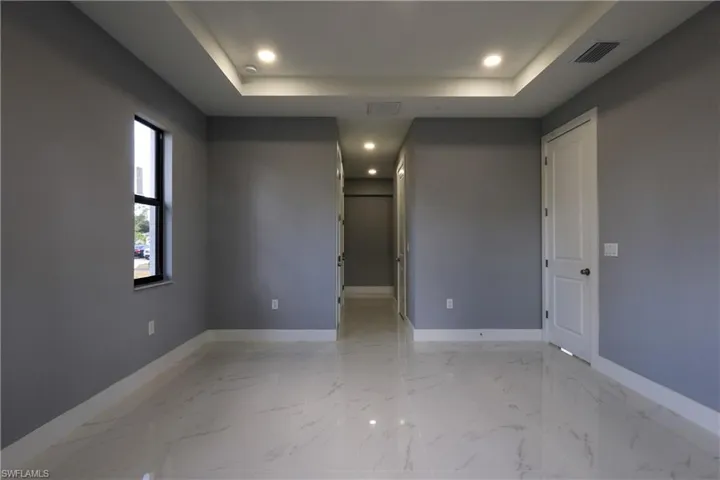Unfurnished room with light marble finish floors, a raised ceiling, and recessed lighting