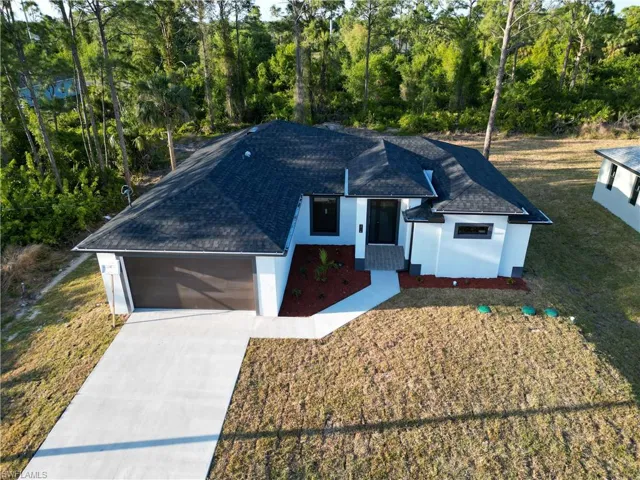 Ranch-style home featuring concrete driveway, a shingled roof, stucco siding, and a front yard