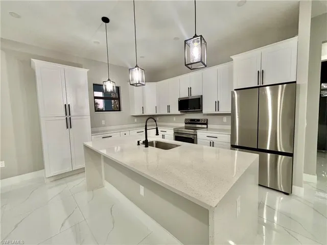Kitchen featuring stainless steel appliances, white cabinets, light stone countertops, decorative light fixtures, and light marble finish flooring
