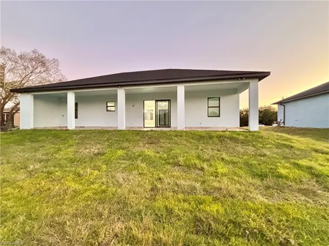 Back of house featuring a lawn and stucco siding