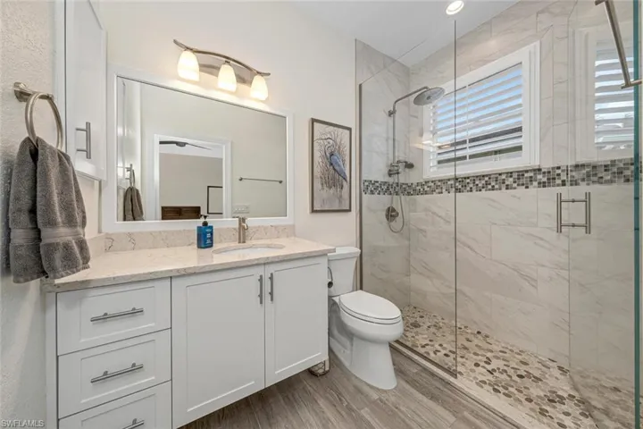 Bathroom with a shower with shower door, vanity, hardwood / wood-style floors, and toilet