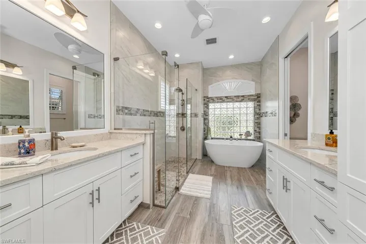 Bathroom with double vanity, separate shower and tub, wood-type flooring, and ceiling fan